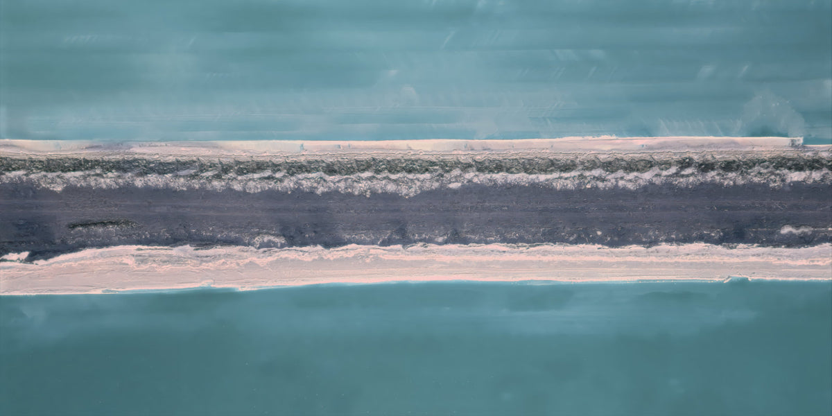 Aerial abstract representation of a narrow strip of pale sand and dark vegetation between two large areas of turquoise water.