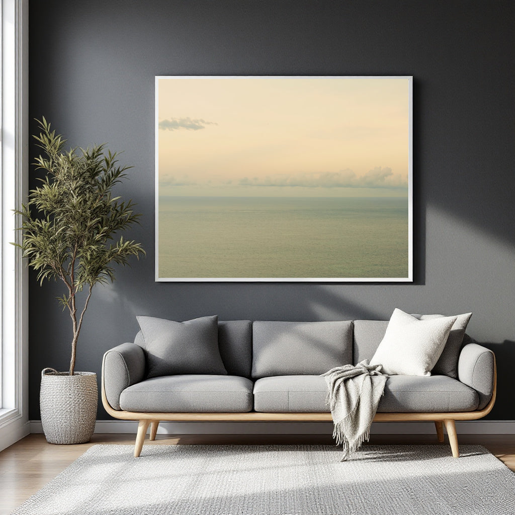 A framed minimalist landscape art print featuring a soft beige sky and muted green sea, displayed on a dark gray wall above a modern gray sofa in a styled living room.
