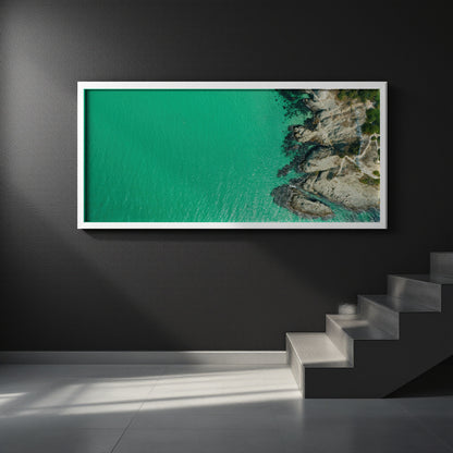 A framed aerial photograph of a turquoise sea meeting rocky coastline, displayed on a dark gray wall above a modern staircase.