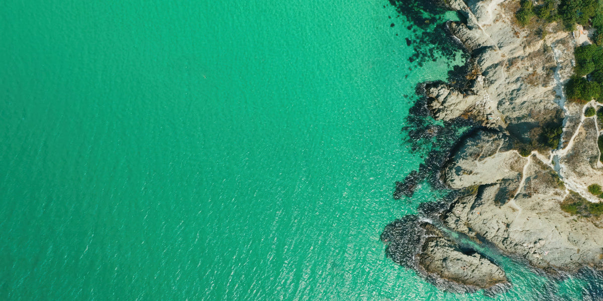 Aerial view of turquoise ocean water meeting a rocky coastline with sparse green vegetation.