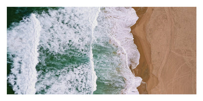 Aerial view of ocean waves with white foam rolling onto a sandy beach, shown as a square print or artwork with a thin white border.