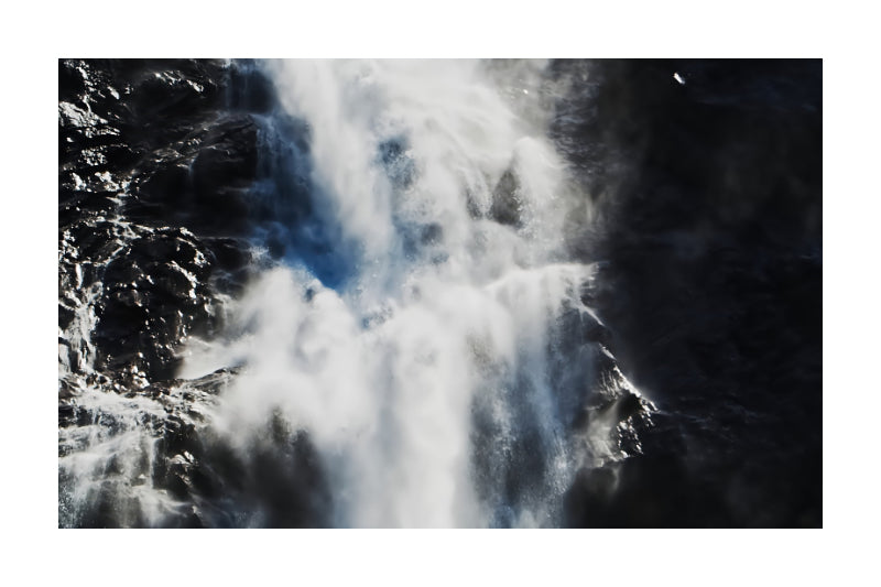 A square photographic print of a powerful waterfall cascading down dark, rocky cliffs, surrounded by a clean white border.