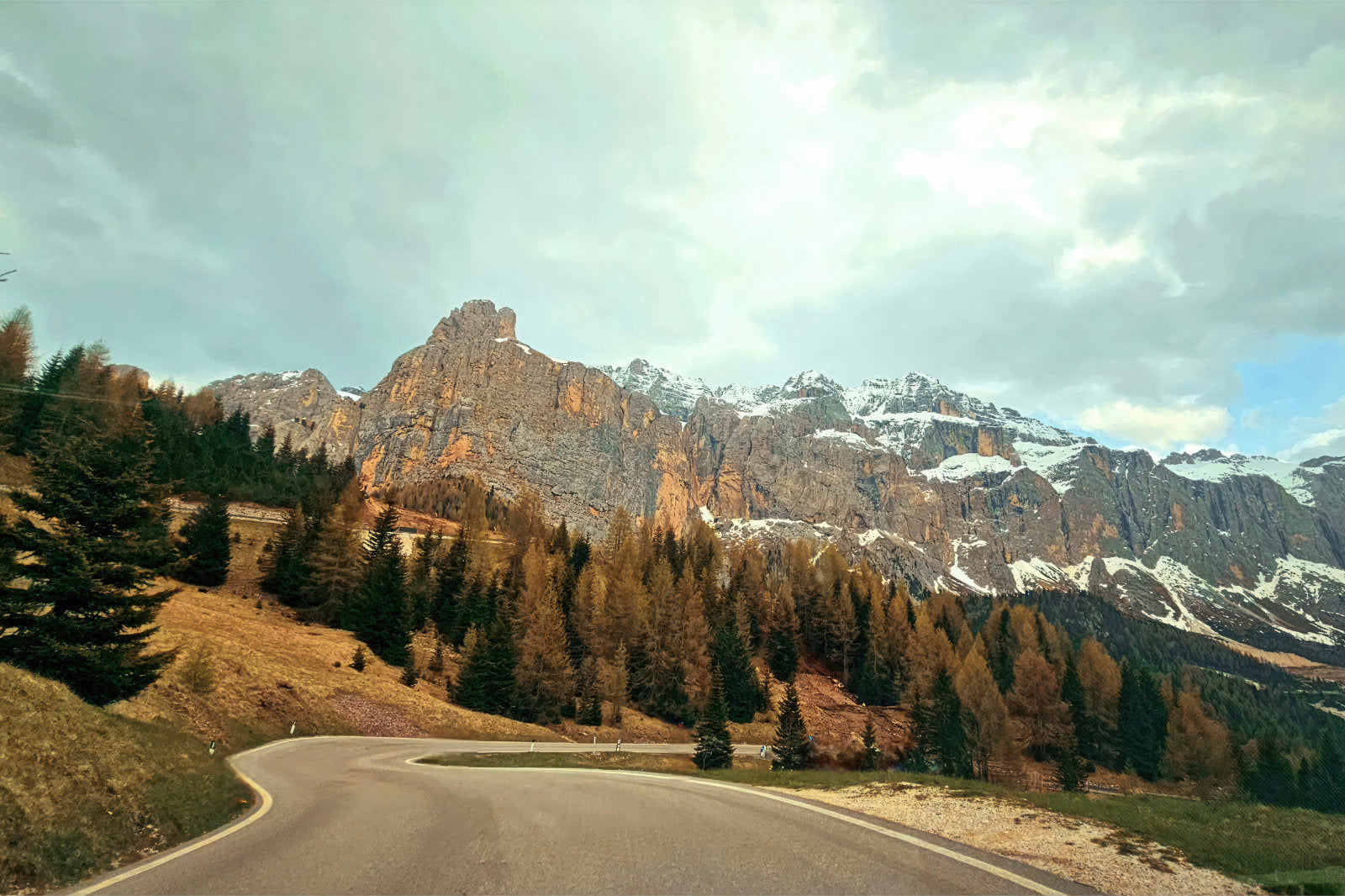 Road going through the Dolomites mountains. The scenic road shows the rocky mountains dusted in some snow.