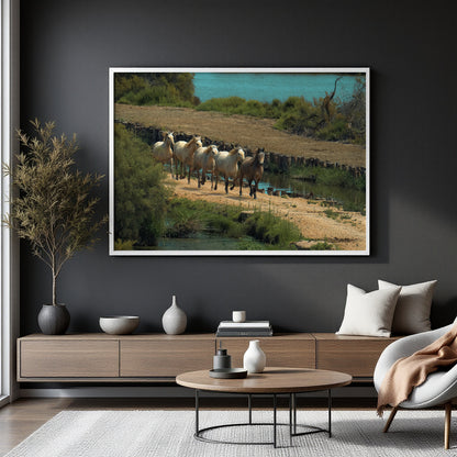 A framed landscape art print depicting a flock of sheep walking along a dirt path near water, displayed on a dark gray wall in a modern styled living room setting.
