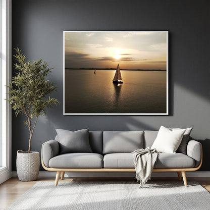 A framed wall art print showing a sailboat on calm water at sunset, displayed above a gray sofa in a modern living room with a potted plant and light-colored rug.
