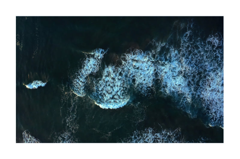 Aerial view of dark ocean water with white surf and foam lines.