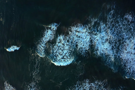 Aerial view of dark ocean water with white sea foam from breaking waves.