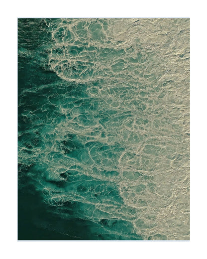 An aerial photograph of ocean waves, showing deep teal water transitioning into white sea foam, presented as a vertical art print with a white border.