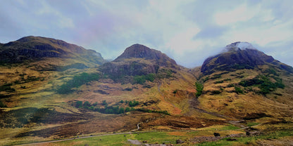 Three rugged Highland peaks rise above a green valley beneath a moody sky