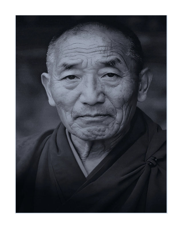 A black and white portrait photograph of an elderly man with deep facial wrinkles, wearing dark robes, presented as a square art print with a white border.