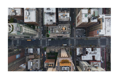Aerial photograph of a dense urban cityscape with intersecting streets, buildings, rooftops, and crosswalks, shown with a white border around the print.