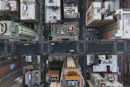 Aerial top-down photograph of a dense city street grid with surrounding buildings, roads, crosswalks, and rooftops.