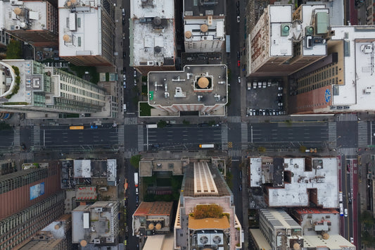 Aerial top-down photograph of a dense city street grid with surrounding buildings, roads, crosswalks, and rooftops.