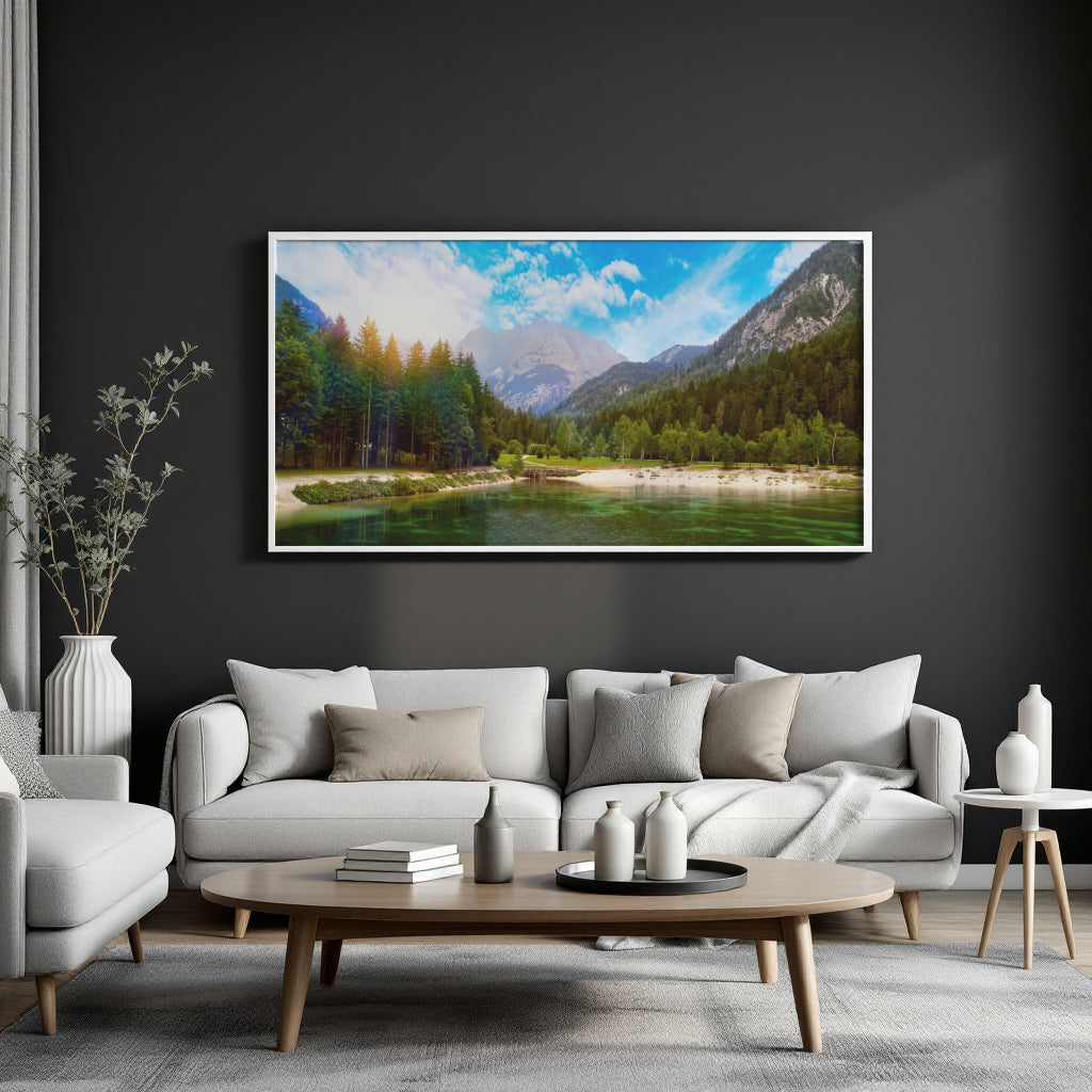 A framed landscape art print depicting a scenic mountain lake with green forests and blue sky, displayed on a dark charcoal wall above a modern light gray sofa in a styled living room.