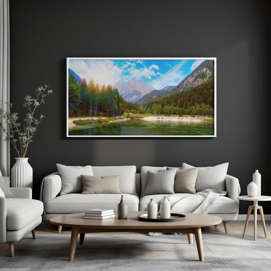 A framed landscape art print depicting a scenic mountain lake with green forests and blue sky, displayed on a dark charcoal wall above a modern light gray sofa in a styled living room.