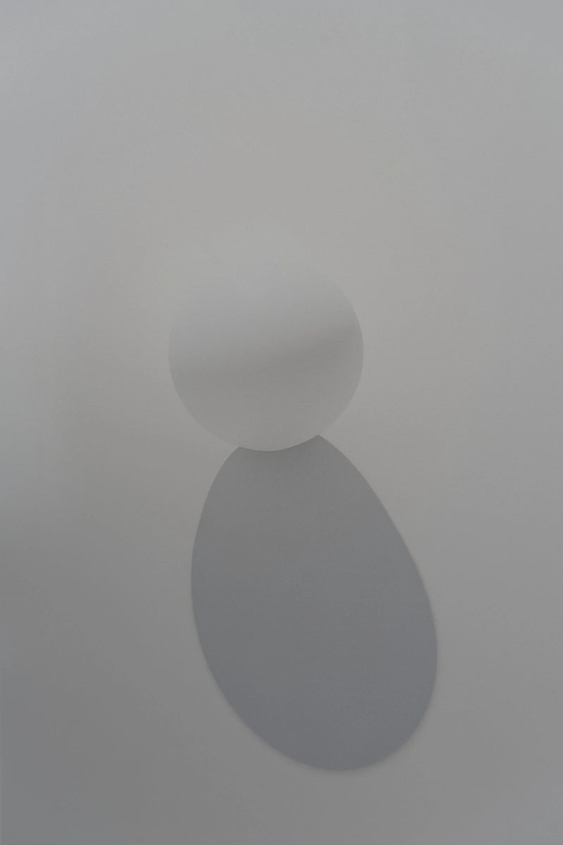 A minimalist white wall sconce featuring a spherical table tennis ball casting a soft, downward-facing oval shadow against a clean, light gray wall.