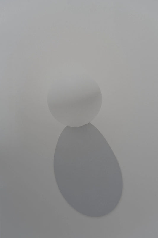 A minimalist white wall sconce featuring a spherical table tennis ball casting a soft, downward-facing oval shadow against a clean, light gray wall.