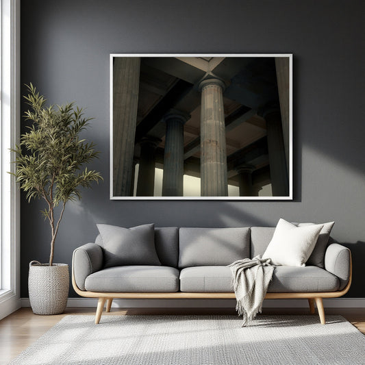 A framed wall art print depicting classical stone columns under a bridge, displayed on a dark gray wall above a modern gray sofa in a styled living room.