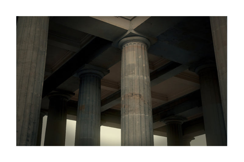 A photograph of classical stone columns and a coffered ceiling inside a grand building, framed with a white border.