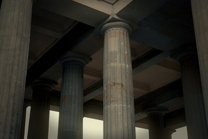 A low-angle view of classical stone columns supporting a dark ceiling in a grand interior space.