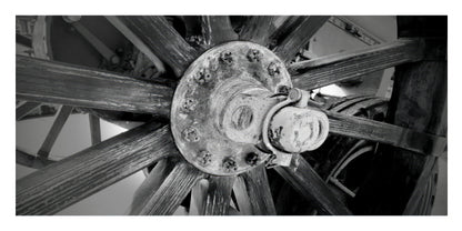 Black and white close-up photograph of a large wooden spoked wheel hub with visible bolts and aged wood texture.