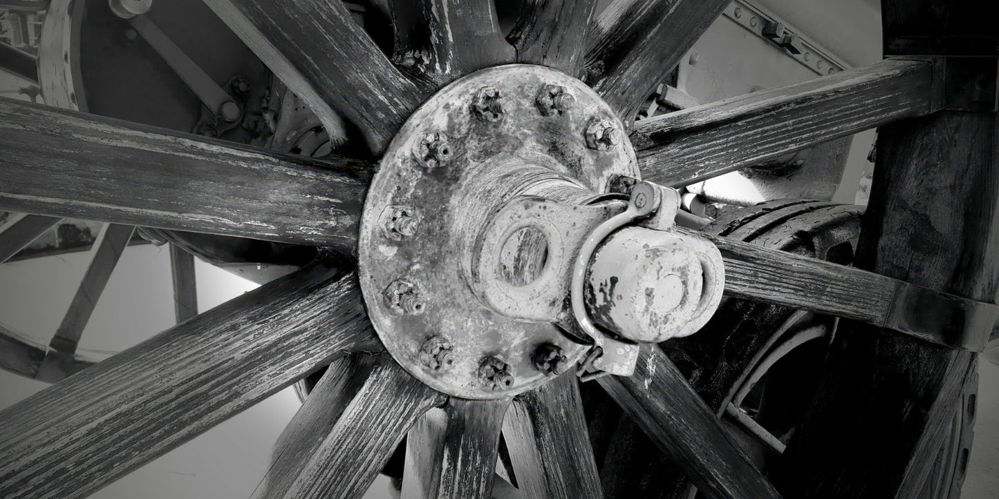 Black and white close-up photograph of a rustic wooden spoked wheel with a central metal hub and bolts.