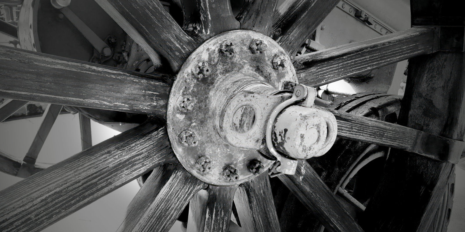 Black and white close-up photograph of a rustic wooden spoked wheel with a central metal hub and bolts.