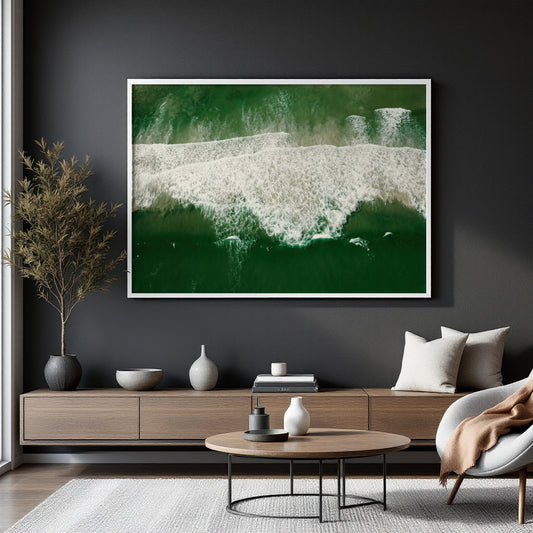 A framed wall art print showing an aerial view of green ocean waves with white foam, displayed in a modern living room setting above a wooden console table.