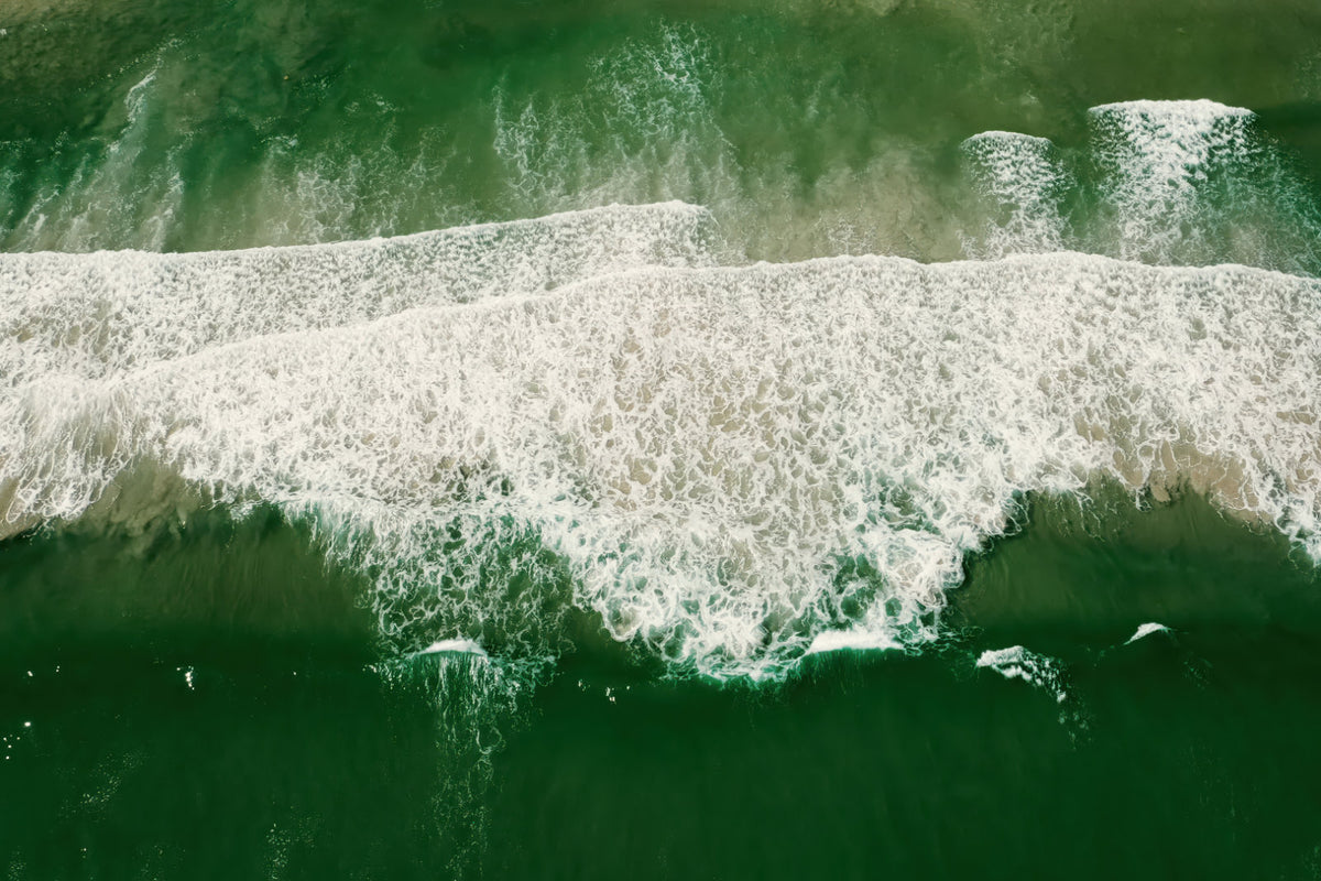 Aerial view of green ocean waves with white foam rolling across the water.