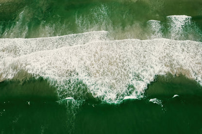 Aerial view of green ocean waves with white foam rolling across the water.