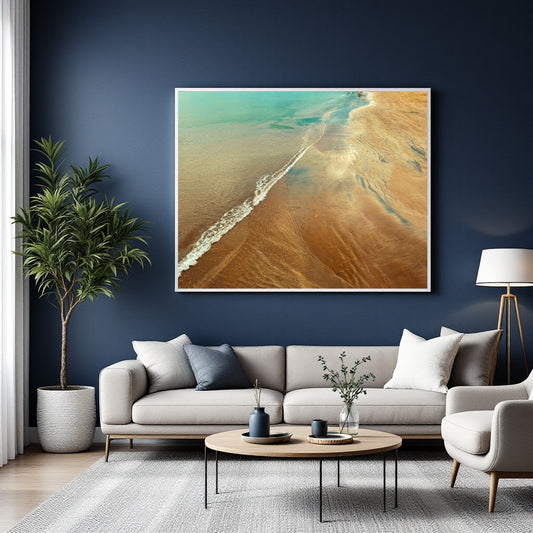 A large framed abstract beach art print hangs on a dark navy wall above a light gray sofa in a modern living room setting.