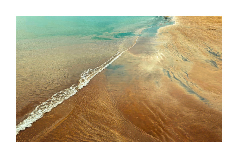 A square art print depicting an aerial view of a beach shoreline, showing turquoise water meeting golden-brown sand in a diagonal pattern.
