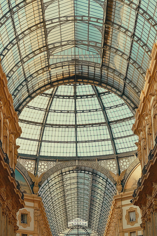 An upward view inside a grand arched glass pavilion with ornate beige stone columns and a metal grid roof.