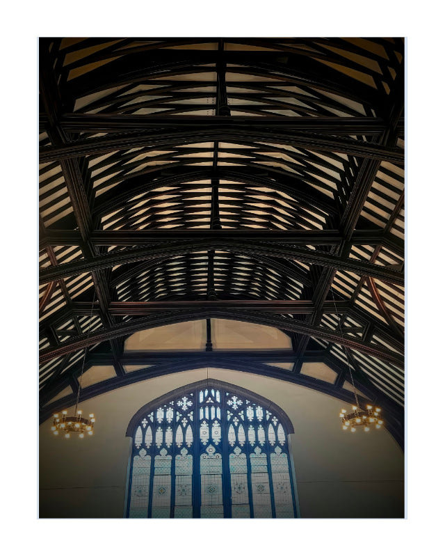 A vertical art print depicting the interior of a historic church or cathedral, looking up at a massive dark wood roof truss system with a large stained glass window at the bottom.