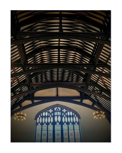 A vertical art print depicting the interior of a historic church or cathedral, looking up at a massive dark wood roof truss system with a large stained glass window at the bottom.
