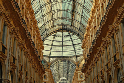 The grand arched glass and metal roof of the Galleria Vittorio Emanuele in Milan, overlooking ornate beige stone arcade buildings on both sides.