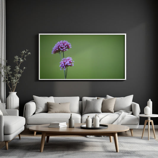 A framed wall art print featuring two purple flower clusters on a green background, displayed above a light gray sofa in a modern living room setting.