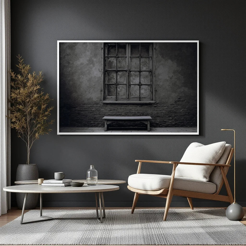 A black and white fine art photograph of an old stone wall with a large multi-paned window and a simple wooden bench below it, presented with a white border.