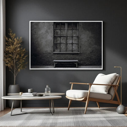 A black and white fine art photograph of an old stone wall with a large multi-paned window and a simple wooden bench below it, presented with a white border.
