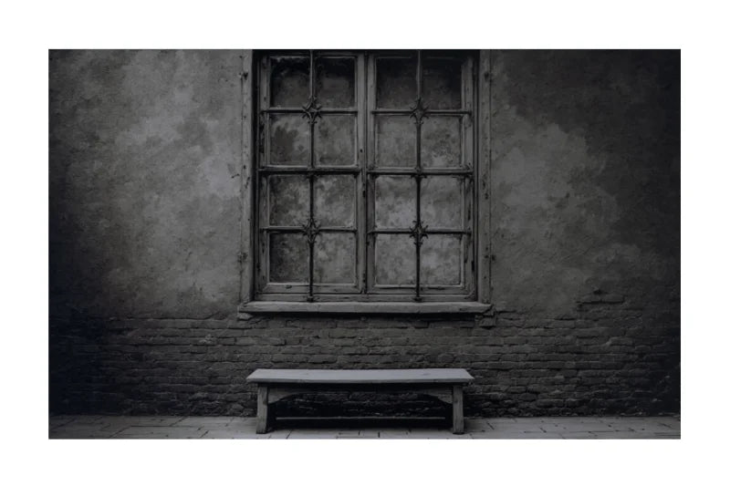 A large framed black and white photograph of an old window and bench mounted on a dark gray wall in a modern living room setting with a wooden armchair, coffee table, and potted plant.