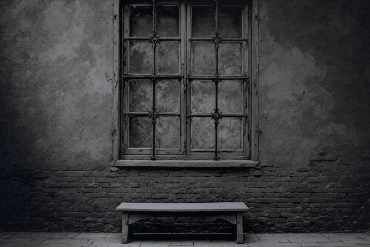 A dark, moody photograph of an old, weathered wooden window with iron bars set into a textured stucco and brick wall, with a simple wooden bench on the floor below.