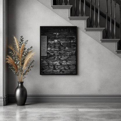 A black and white framed art print depicting a rustic stone wall with ducks, displayed on a light gray wall in a modern staircase landing next to a black vase with dried pampas grass.