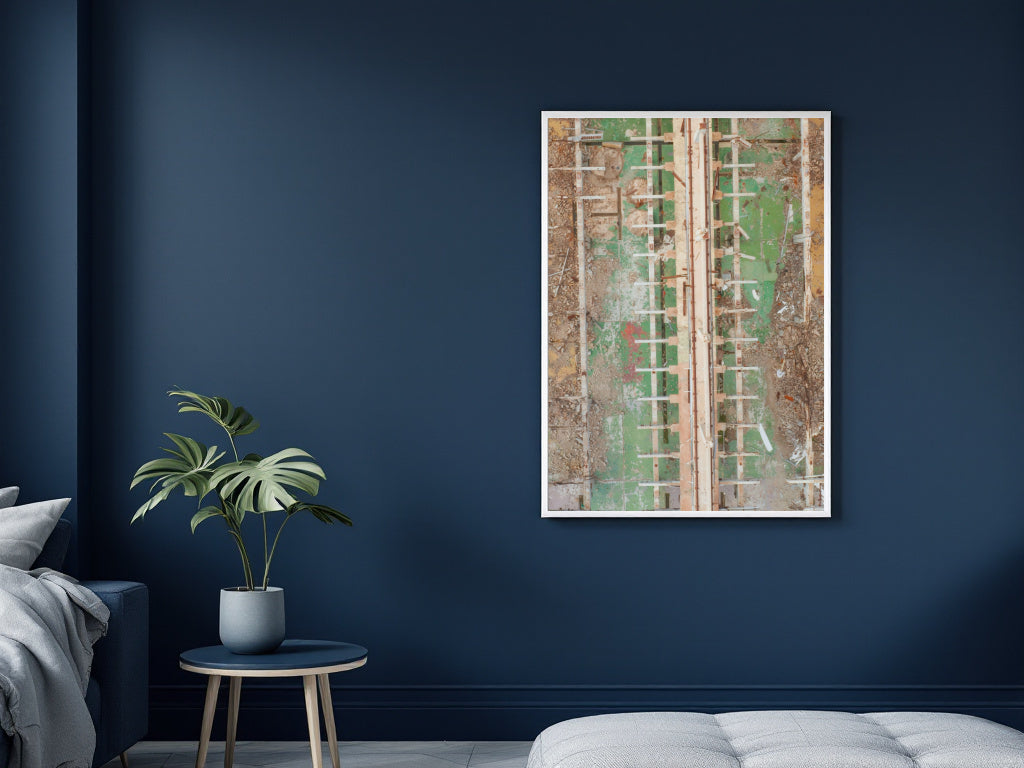 A framed abstract art print featuring textured vertical panels in green, beige, and brown tones, displayed on a dark navy blue wall in a modern bedroom setting next to a potted plant and a white tufted bench.
