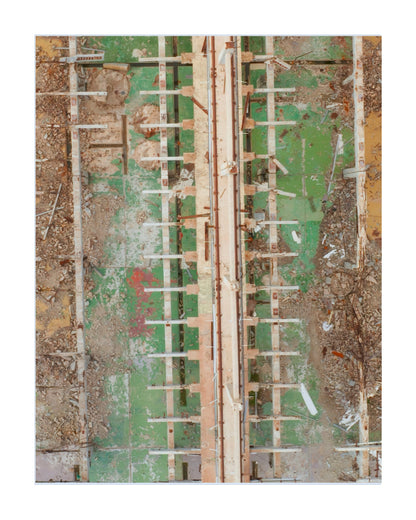 An aerial-style overhead photograph of a construction or demolition site with exposed wooden formwork, rebar, and a weathered green and tan ground surface.