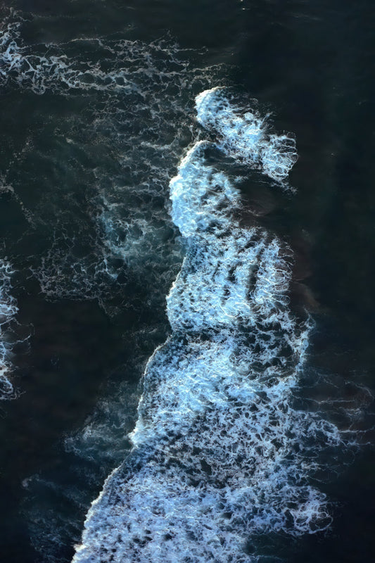 Aerial view of dark ocean water with a strong diagonal white surf wave cutting through the surface.