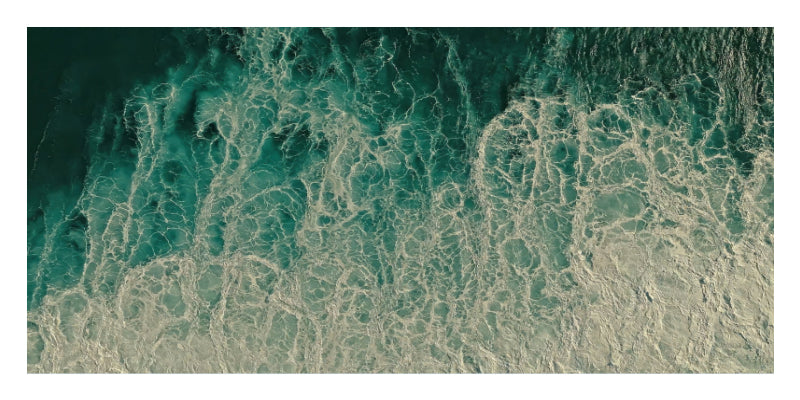 An aerial-style photograph of ocean water with swirling teal, green, and white foam patterns filling the frame.
