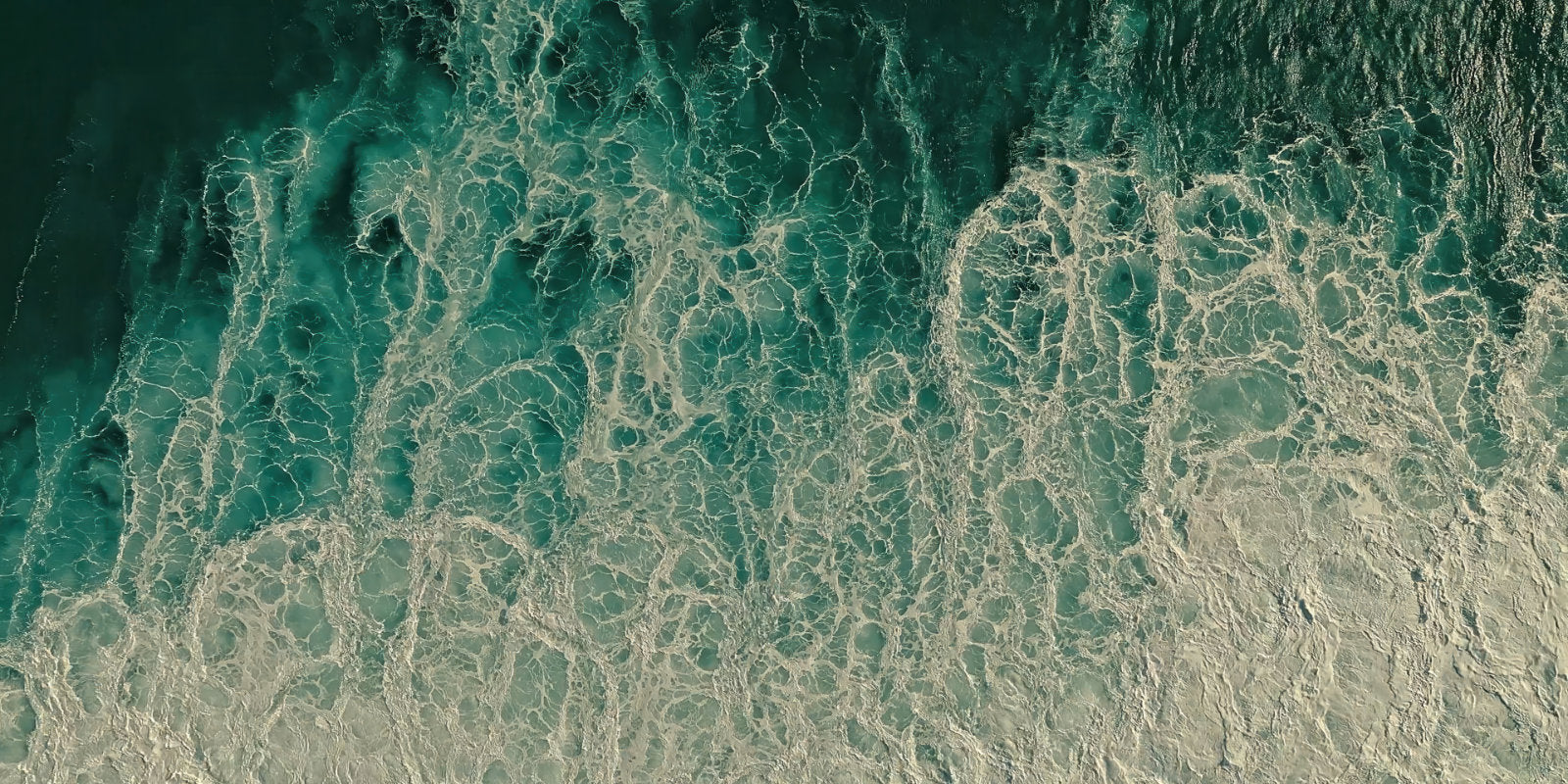 Aerial view of ocean waves with turquoise water and white sea foam, filling the entire frame.