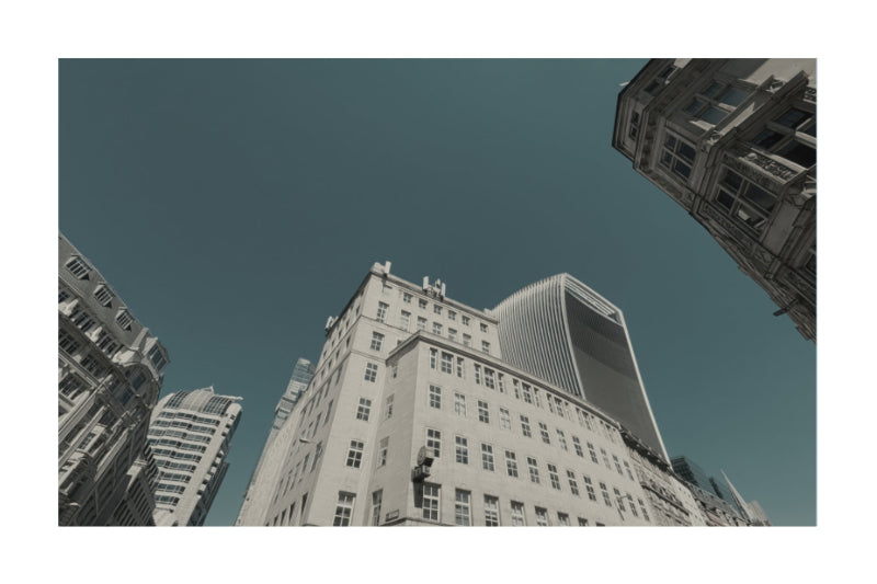 A low-angle photograph of tall city buildings against a deep teal-blue sky, presented with a white border.