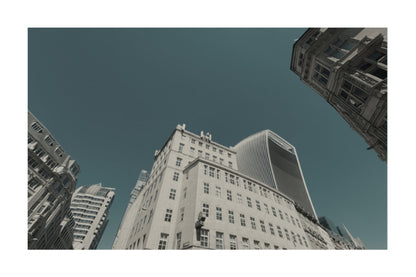 A low-angle photograph of tall city buildings against a deep teal-blue sky, presented with a white border.
