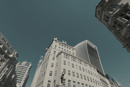 Low-angle photograph of tall city buildings against a muted teal-blue sky, with one large light-colored building centered and other structures framing the edges.